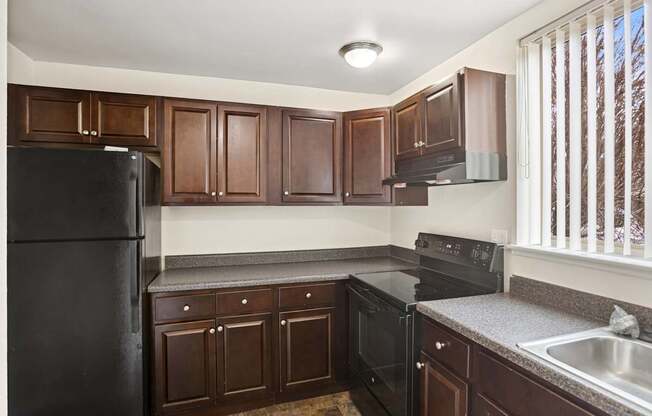 A kitchen with dark wood cabinets and black appliances.