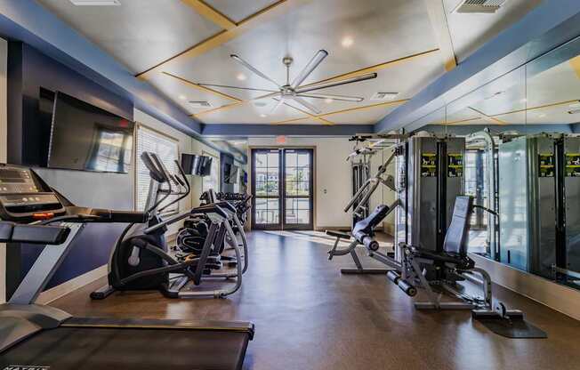 A gym with treadmills, elliptical machines, and a ceiling fan.