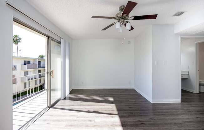 an empty living room with a ceiling fan and a balcony