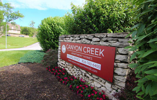 a sign for canyon creek elementary homes in front of a stone wall and plants