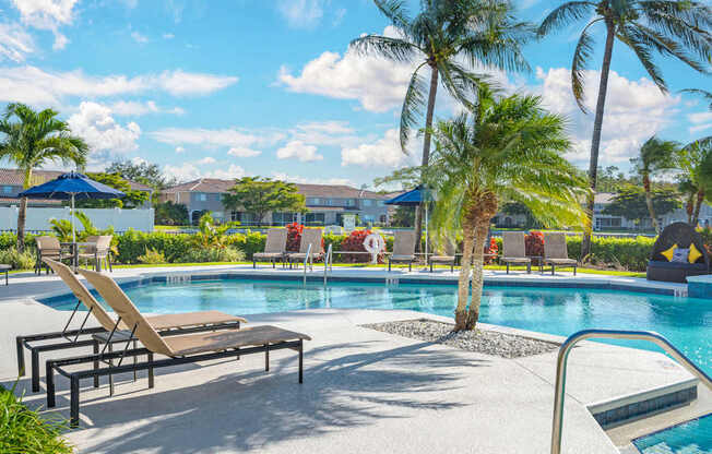 A large outdoor swimming pool with lounge chairs and an adjacent clubhouse overlooking a body of water