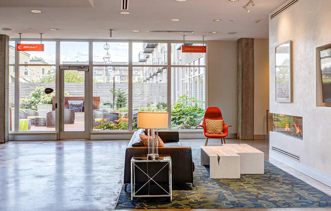 A brightly lit waiting room with a red chair and a table with a lamp on it.