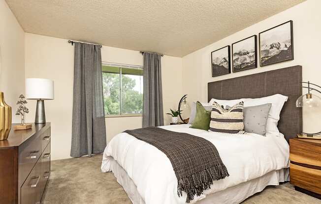 A bedroom with a large bed, a nightstand, and a window with curtains.