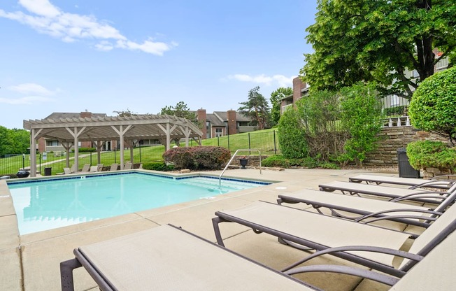 A pool with sun loungers and a pavilion in the background.