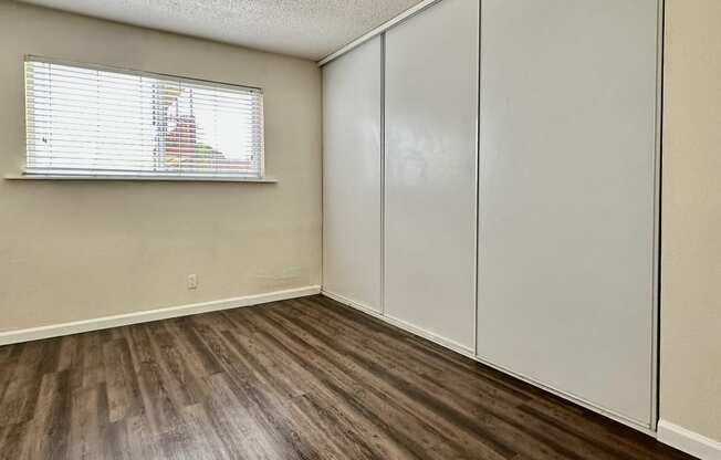 the spacious living room of an apartment with wood flooring and white closets