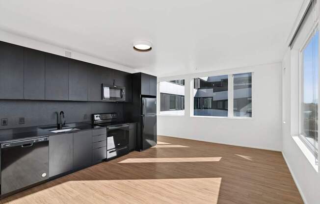 A modern kitchen with dark grey cabinets and a wooden floor.