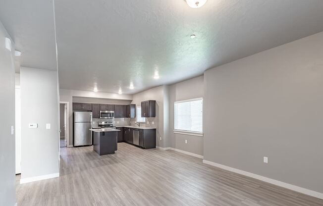 an empty living room with a kitchen in the background