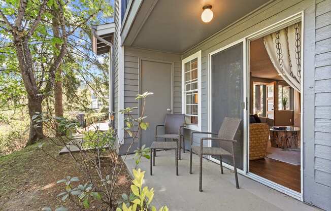 A patio with chairs and a table is on the front porch of a house.