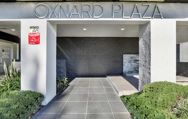 The entrance to Oxnard Plaza is framed by white columns and has a caution sign on the wall.