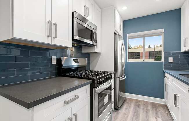 Blue tiled kitchen with stainless steel fridge, oven, and microwave.