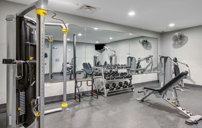 Fitness center with weight machines and dumbbells and a bench at The Vue apartments