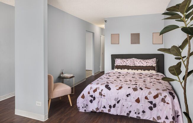 A bedroom with a bed, chair, and plant.