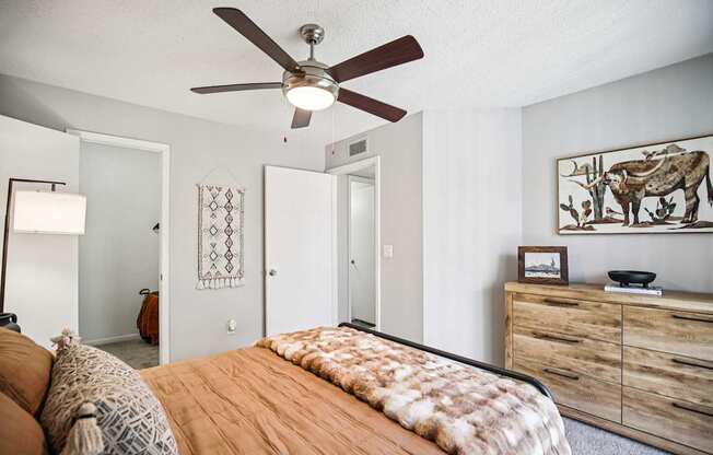 A bedroom with a bed, a ceiling fan, and a dresser.