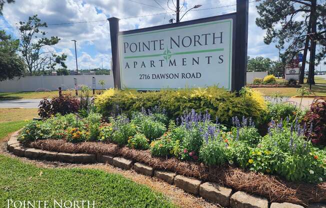 a sign for pointe north apartments in front of a flower garden