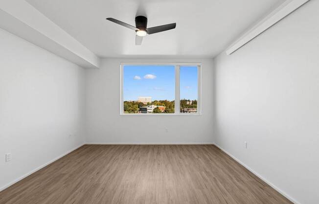 A room with a ceiling fan and a window showing a view of a city skyline.