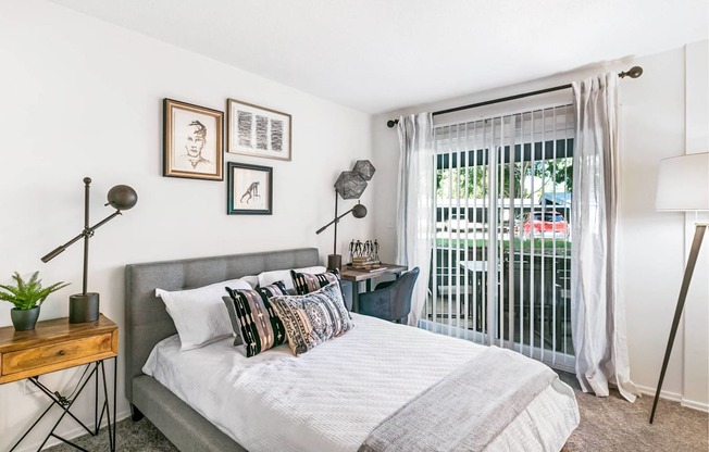 A bedroom with a bed, a nightstand, and a window with a view of a balcony.