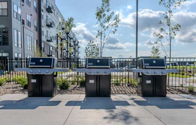 Three trash bins are lined up on a sidewalk in front of a building.