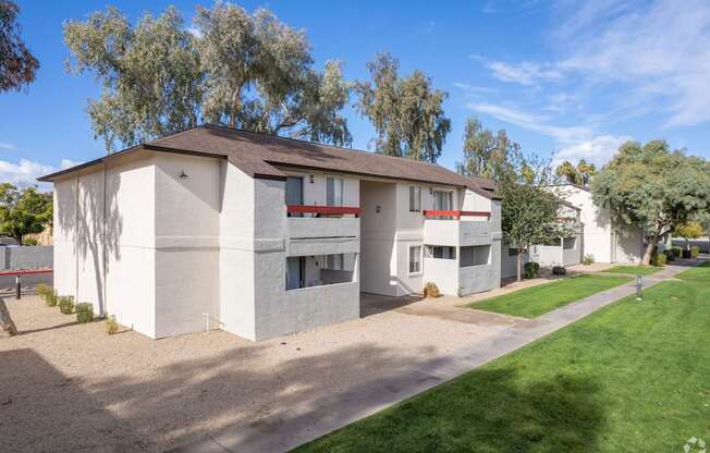 A white building with a brown roof is surrounded by a green lawn.
