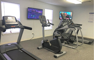 a gym with exercise equipment and televisions in a room