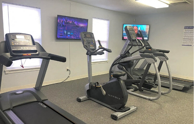 a gym with exercise equipment and televisions in a room