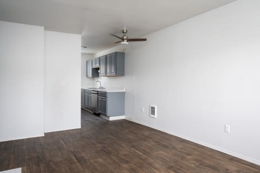 an empty living room with a ceiling fan and a kitchen