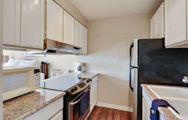 Kitchen with stainless steel electric range over range hood, refrigerator, double kitchen sink, granite countertops wood style floors