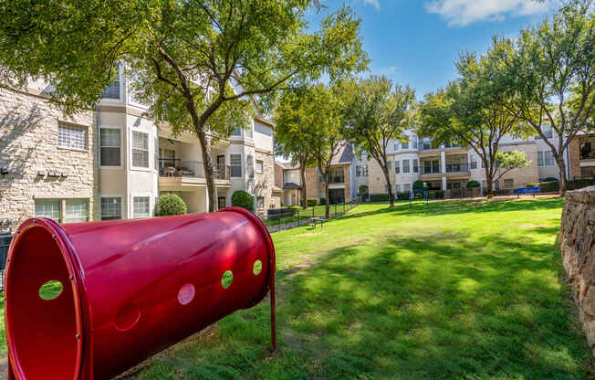 a red mailbox sits in the middle of a grassy area with apartment buildings in the background