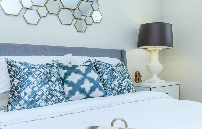 a bedroom with a bed with blue and white pillows   and a lamp