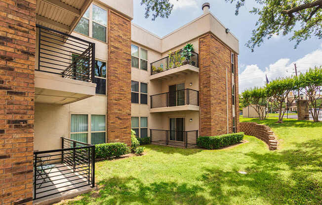 A brick building with a balcony and a green lawn in front.