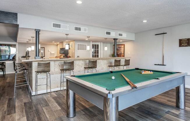 A pool table is in the middle of a room with a bar area.