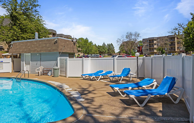 a swimming pool with blue chaise lounge chairs and a poolside building with apartments