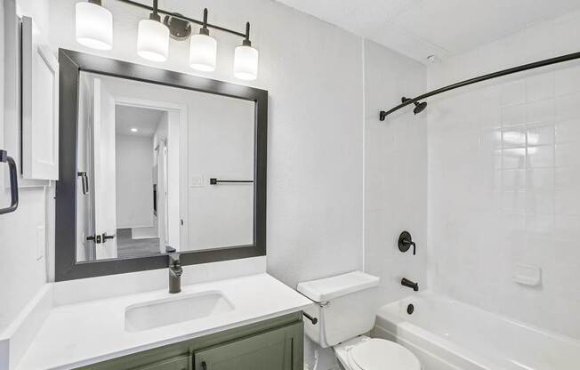 A white bathroom with a green cabinet and a black framed mirror.