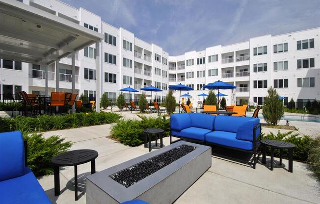 a patio with blue couches and chairs and umbrellas in front of an apartment building