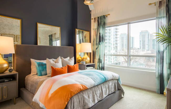 Spacious bedroom with a large bed, full-width window, white walls with a navy accent wall, and beige carpeting.