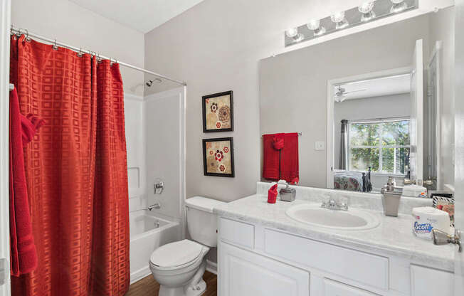 A white bathroom with a red shower curtain.