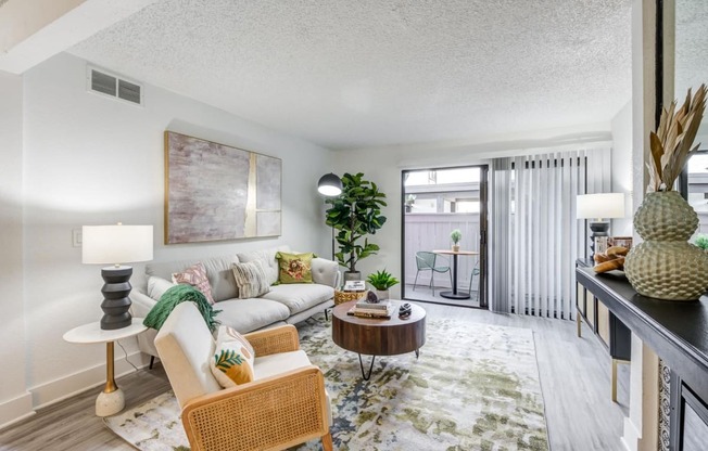 Fusion Warner Center apartments living room with modern grey couch, abstract green and blue rug, and rattan rocking chair with cream cushion.