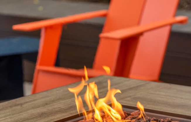 a fire pit on a wooden table with two orange chairs