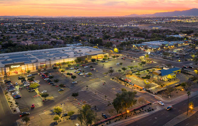 A parking lot with cars and a shopping center in the background during sunset.