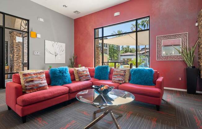 A red couch with blue pillows sits in a room with a glass table in front of it.
