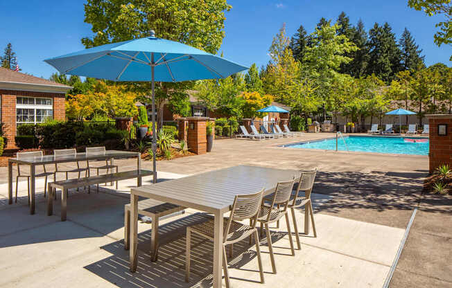 A table and chairs set is arranged on a patio with a pool in the background.