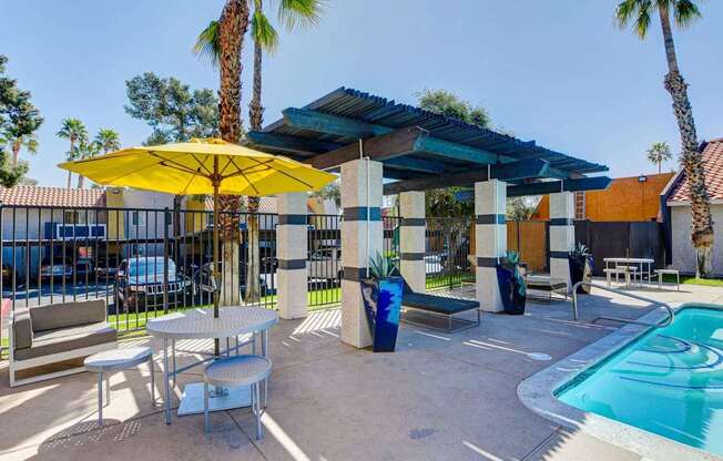 A pool area with a yellow umbrella and a table.
