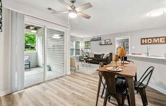 A dining room with a table set for two and a sliding glass door leading to a backyard.