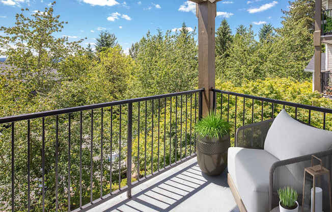 A balcony with a metal railing, a grey couch, and a potted plant.