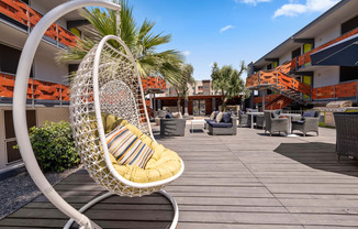 a swing chair sits on a wooden deck in front of a resort with a slide in the