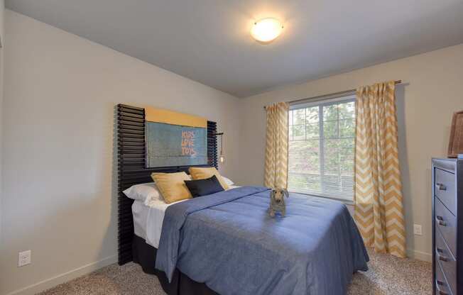 Spare Bedroom with Blue Comforter on Mattress, Open Window, Yellow Blinds, Carpet, Woven Dog,