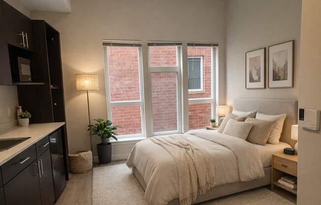 A bedroom with a bed, nightstand, and a window with a view of a brick building outside.