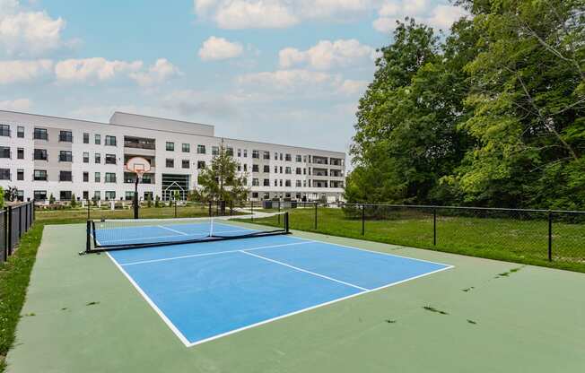 A blue tennis court in front of a white building.
