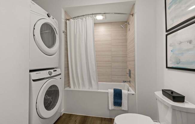 A white washing machine is in a small bathroom with a toilet and a bathtub.