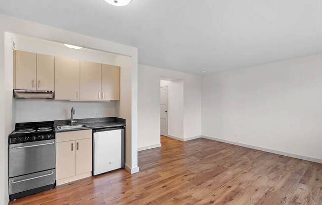 an empty living room with a kitchen with a stove and refrigerator