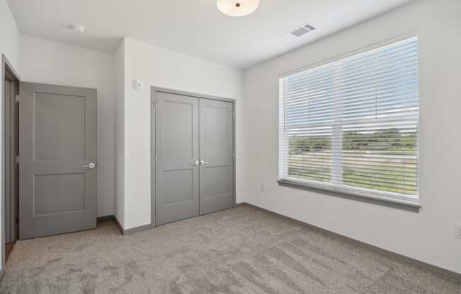 the living room of an apartment with a large window and gray doors at The Depot in The Depot Raymore, MO 64083